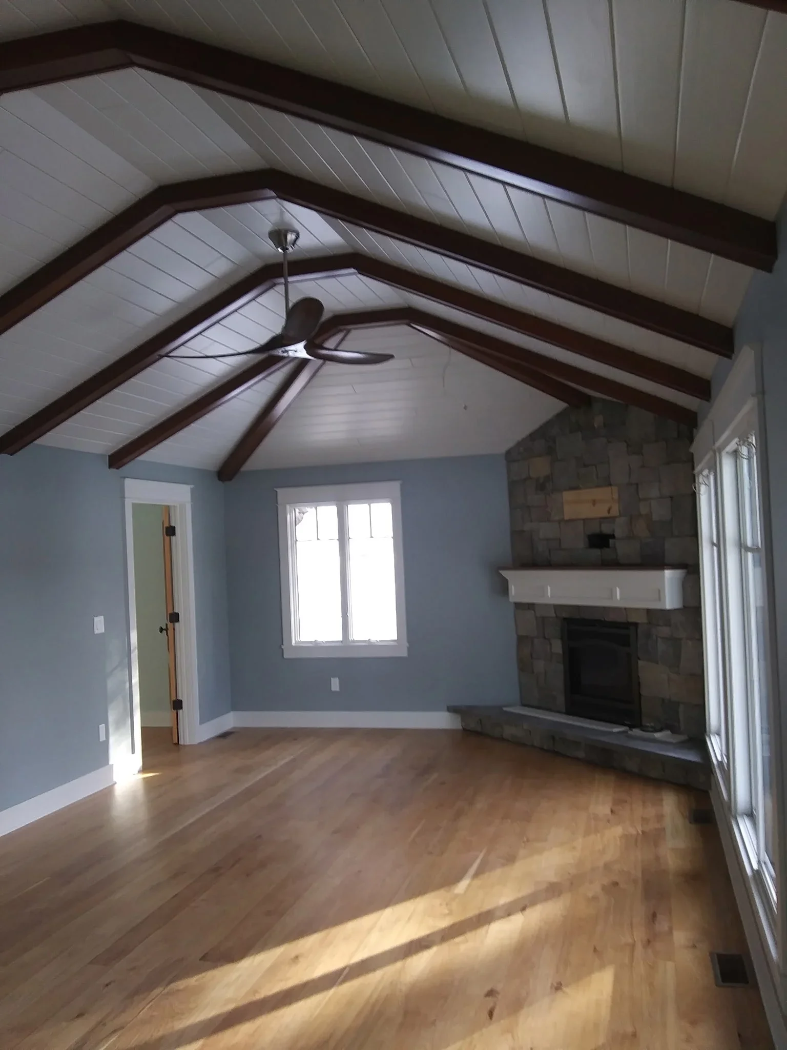 Vaulted ceiling room with blue walls, white shiplap, dark wood beams, and stone fireplace