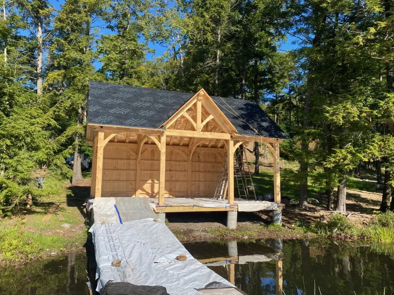 Timber frame boathouse with new charcoal gray shingle roof and exposed beam construction on waterfront
