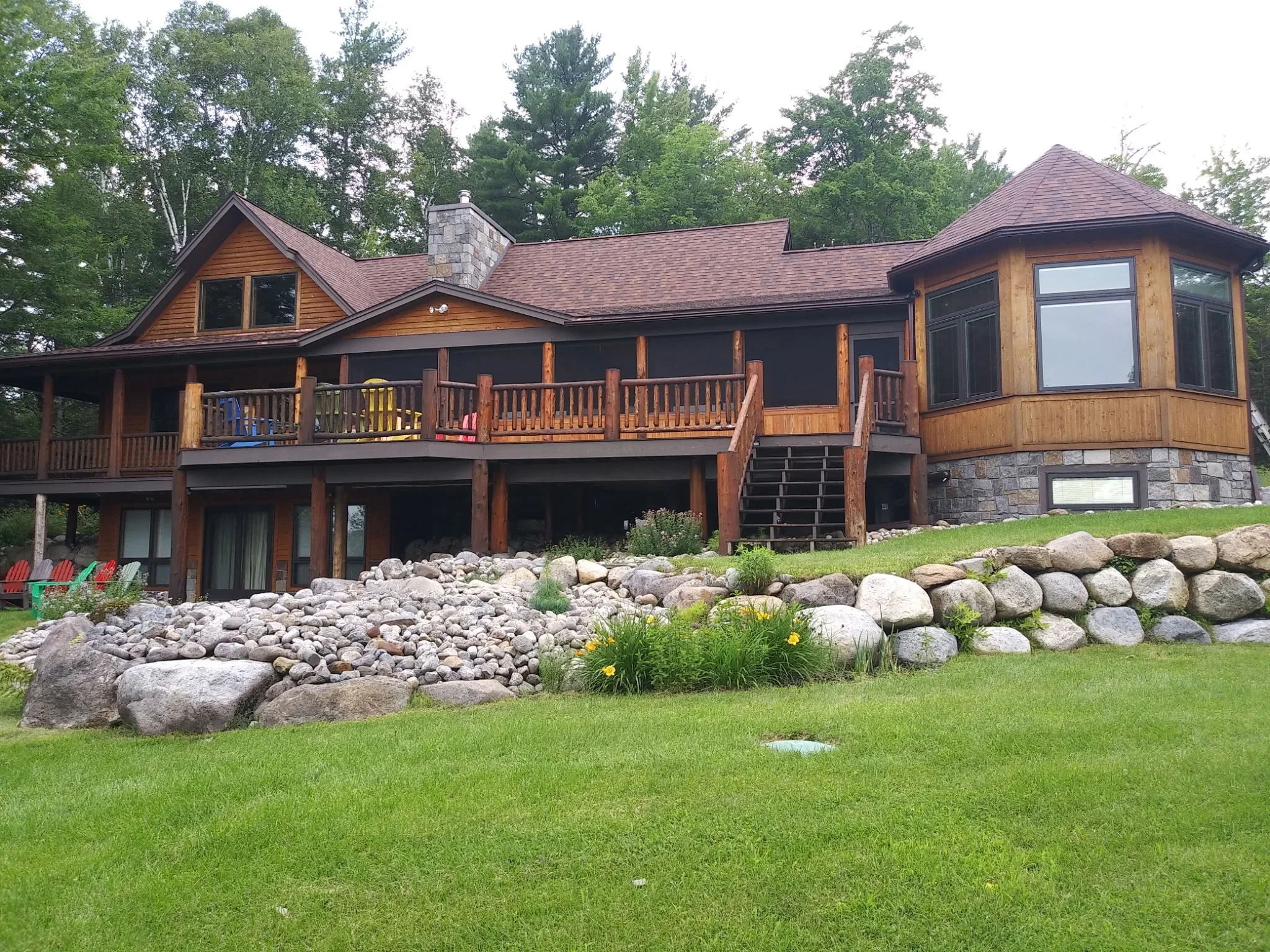 Large residential home with dark stained wood siding, cedar accents, and multi-level decks overlooking landscaped grounds