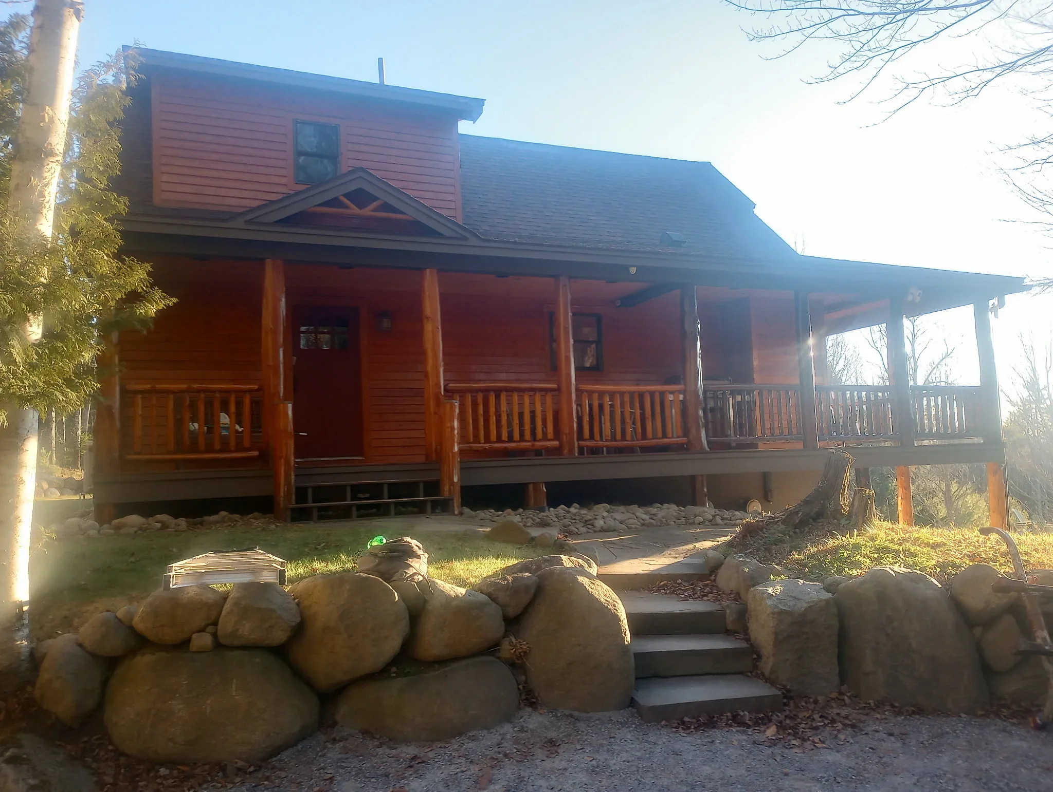 Rustic log cabin with reddish-brown stained exterior, dark roof trim, and covered front porch with wooden railings