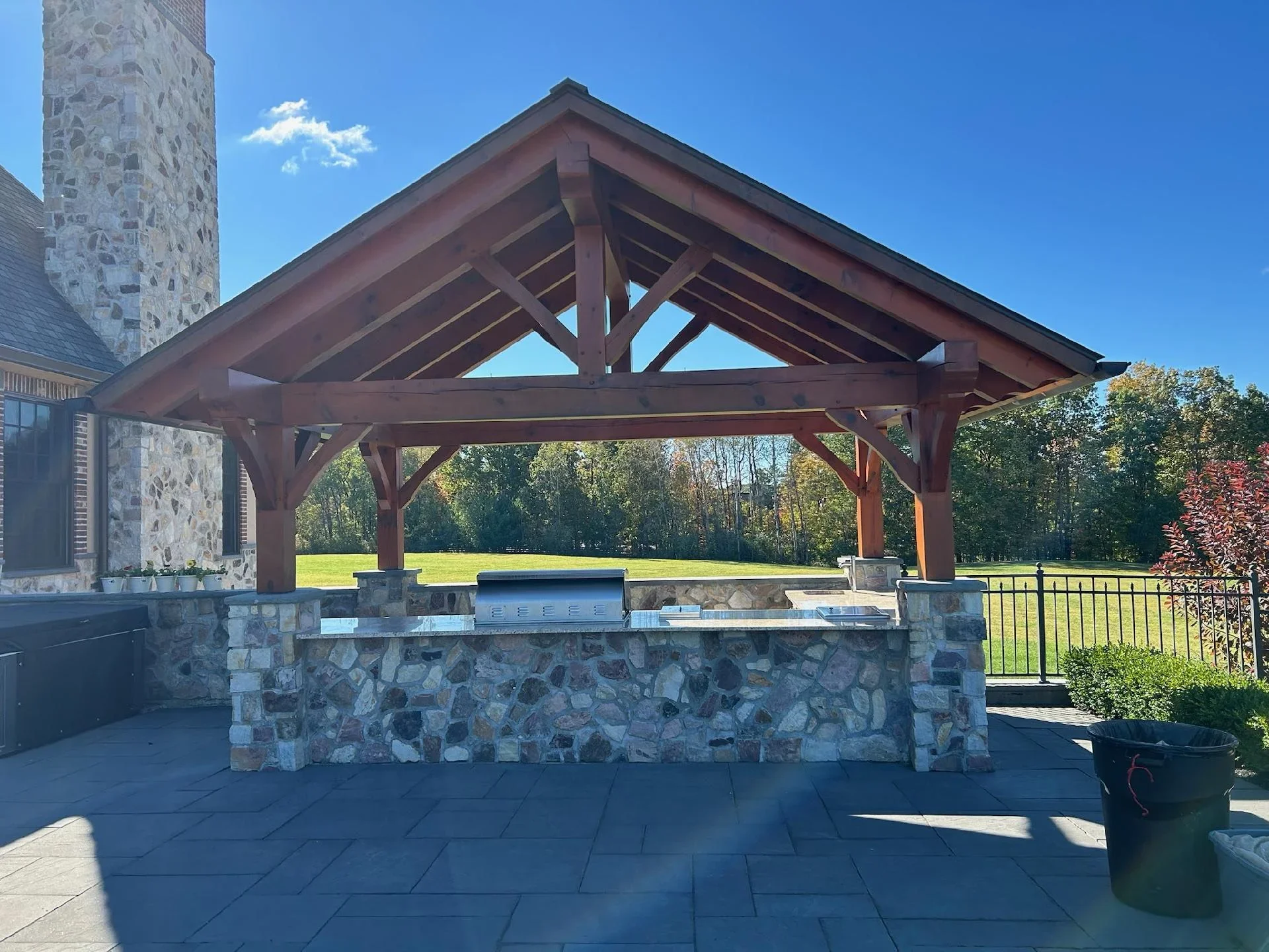Burgundy stained timber pergola with stone outdoor kitchen and slate patio