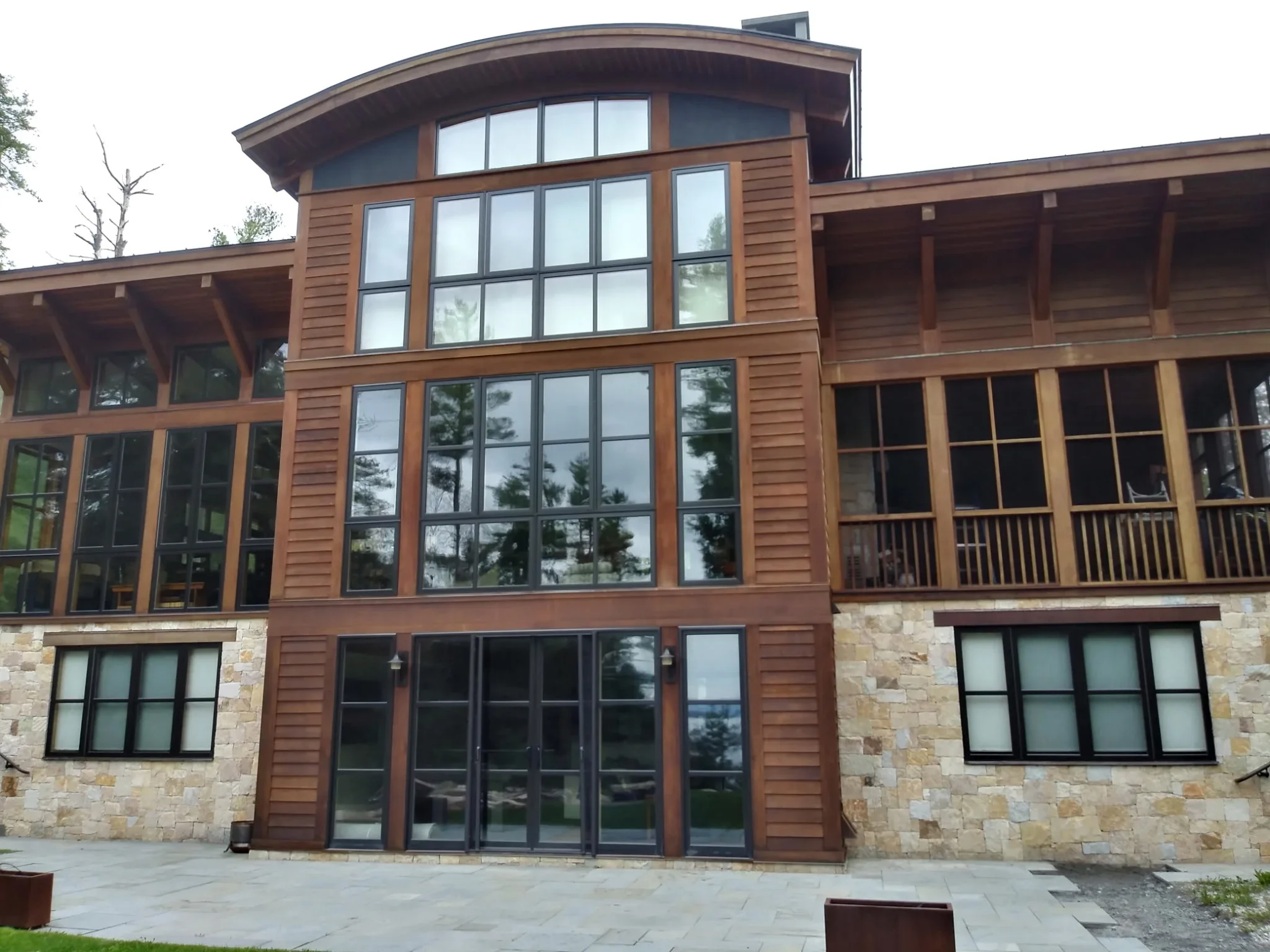 Contemporary home with reddish-brown painted wood siding, stone base, and large multi-pane windows