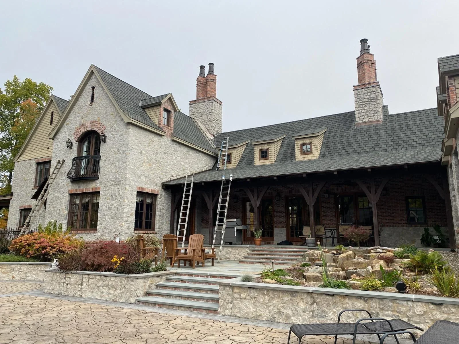Stone and brick estate home with painted exterior, covered porch, and manicured landscaping