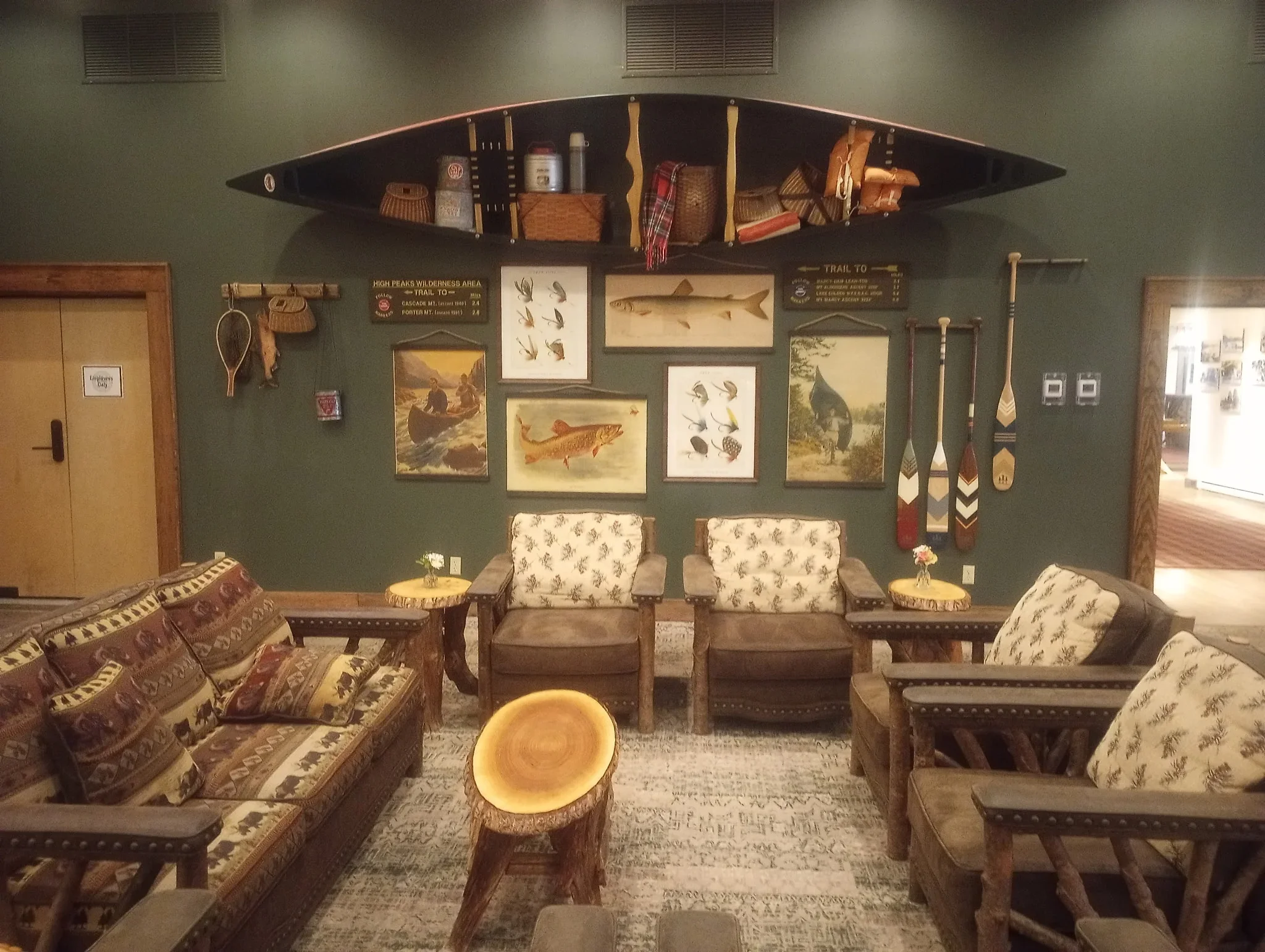 Sage green painted lodge interior with wood furniture, fishing memorabilia, and canoe display