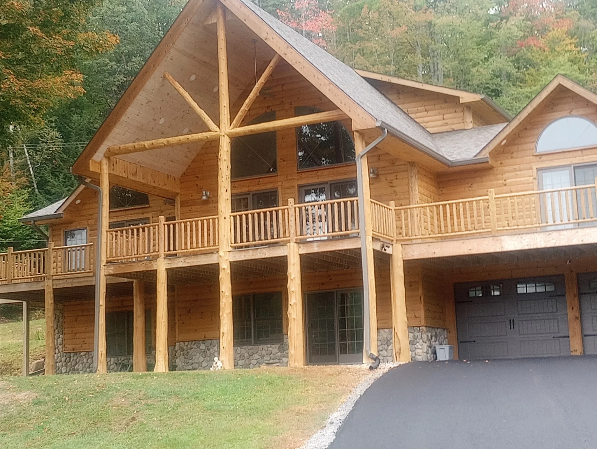 Large log home with stained timber exterior, stone foundation, and wrap-around deck