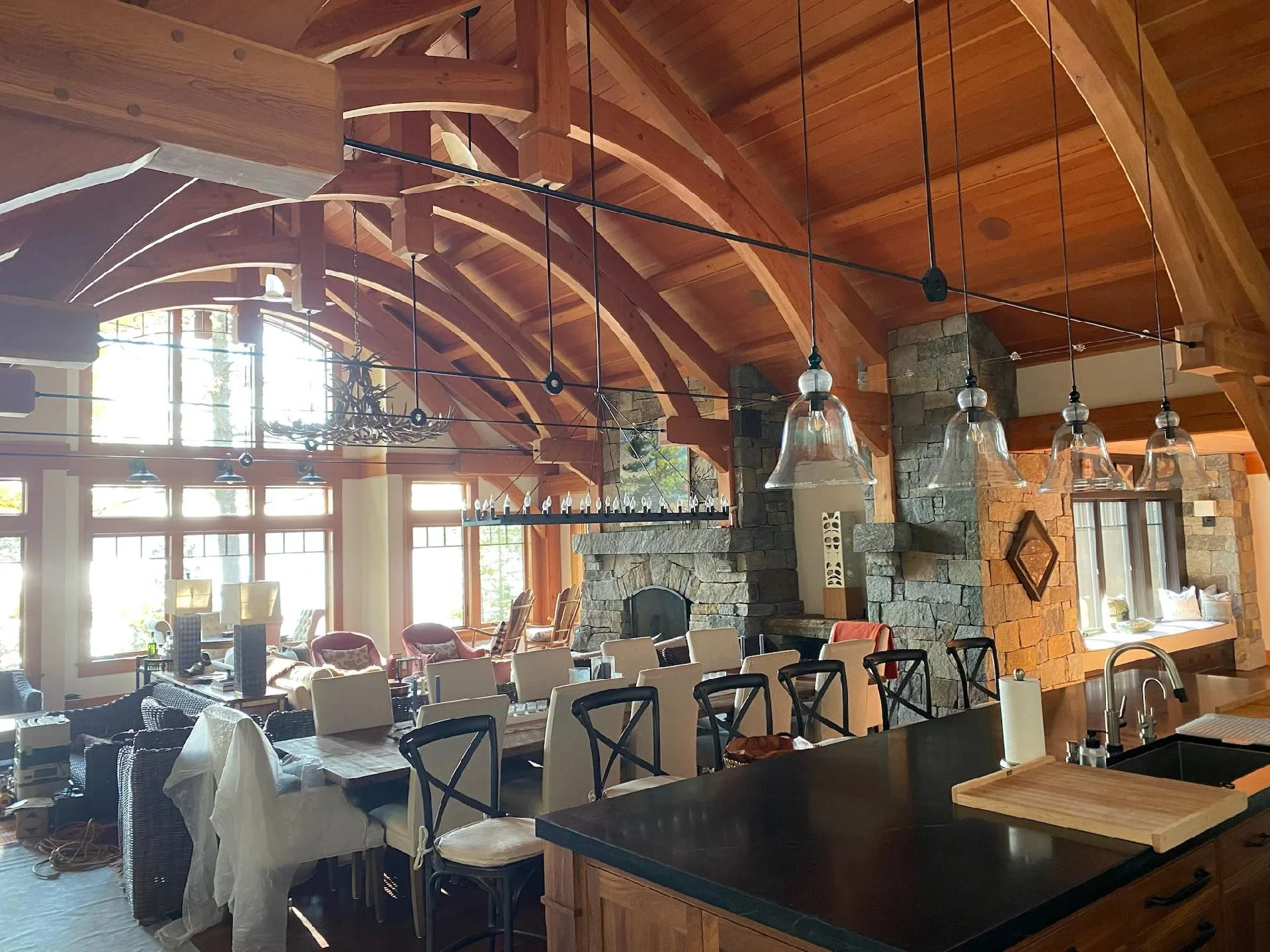 Painted open-concept great room with timber ceiling, stone fireplace, and pendant lighting