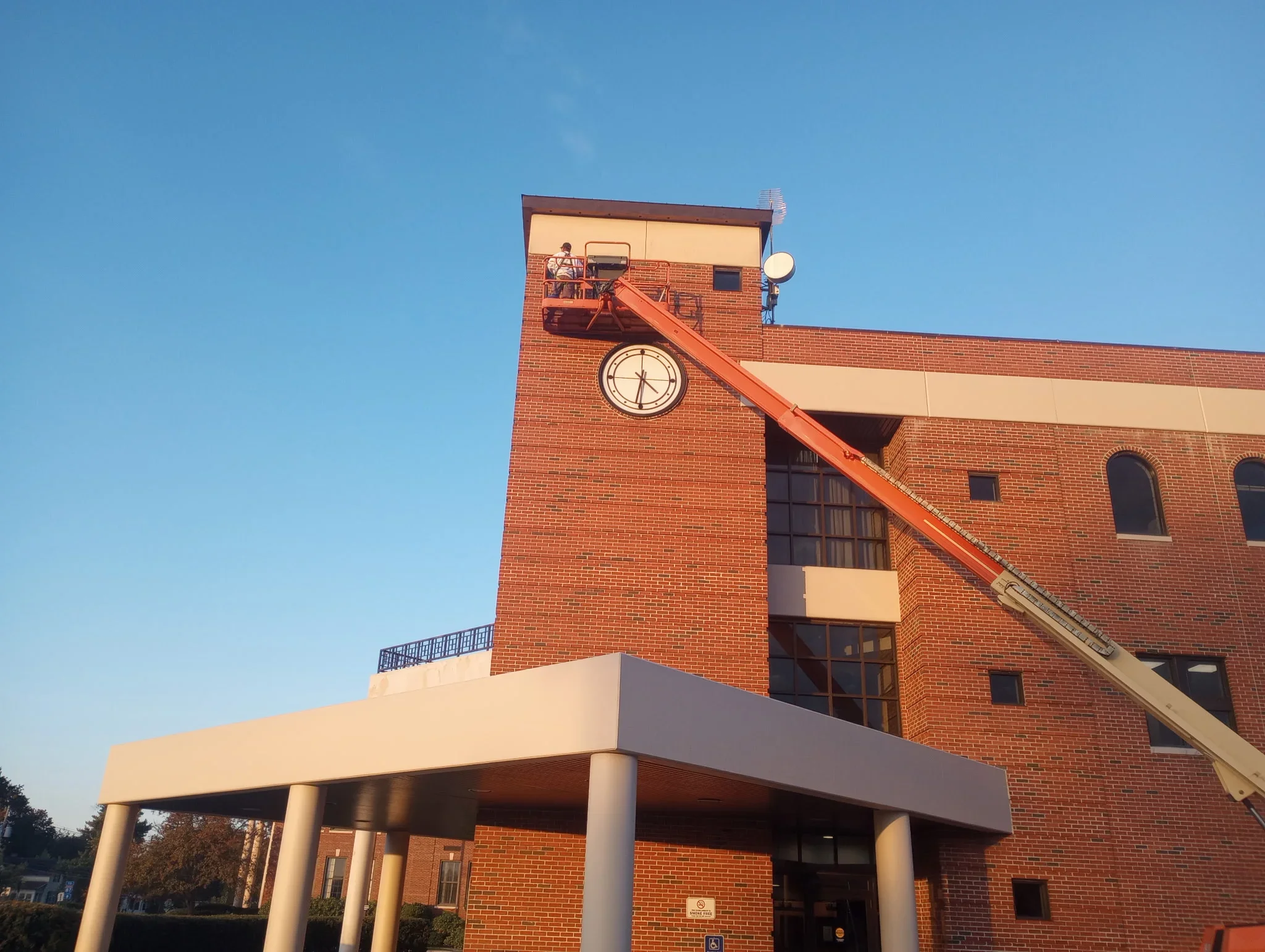 Brick commercial building with cream-colored painted trim and clock tower, elevated work platform visible
