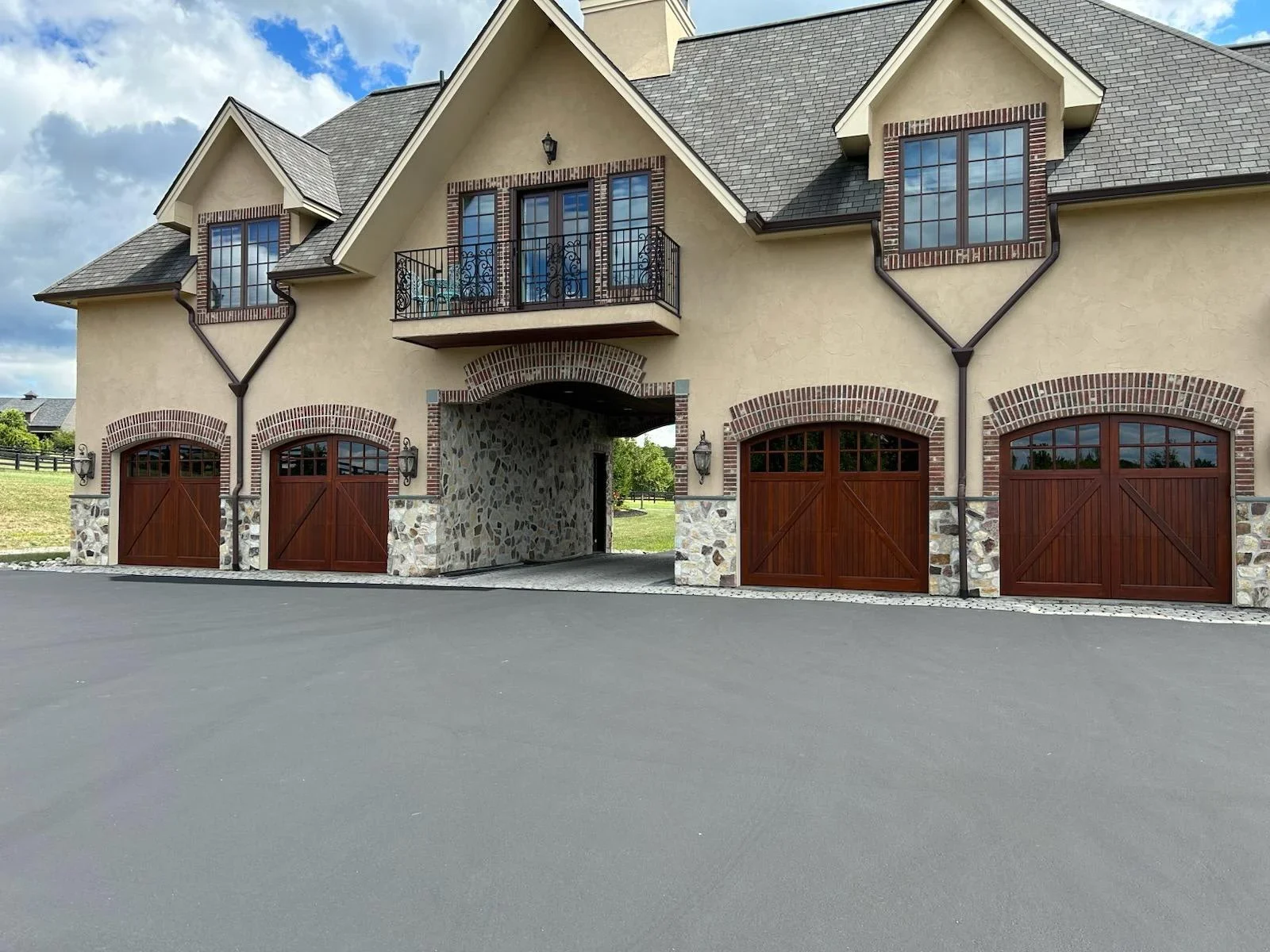 Cream stucco home with gray roof, brick archways, and dark wood garage doors