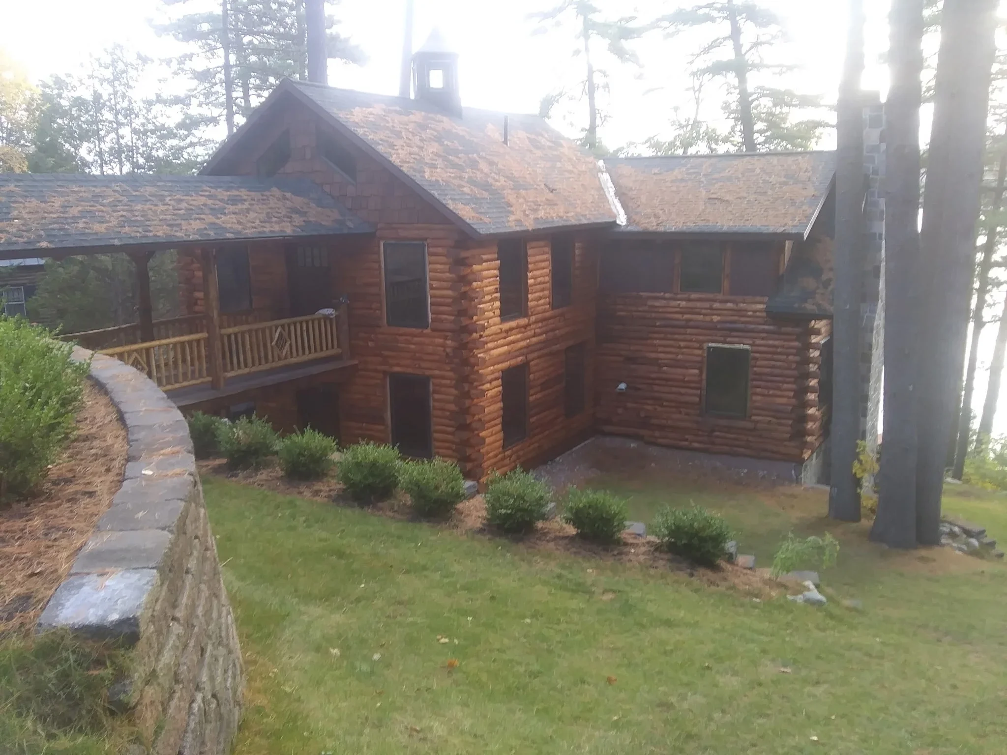 Rustic log cabin with stained wood siding, gabled roof, and wooden deck surrounded by tall pines
