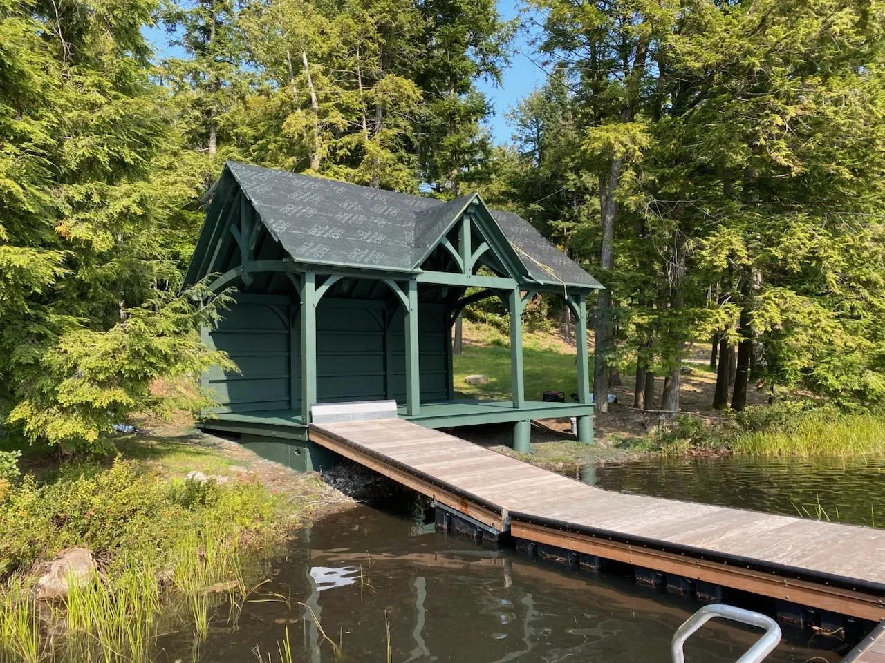Green painted boathouse with dock on calm water surrounded by forest trees