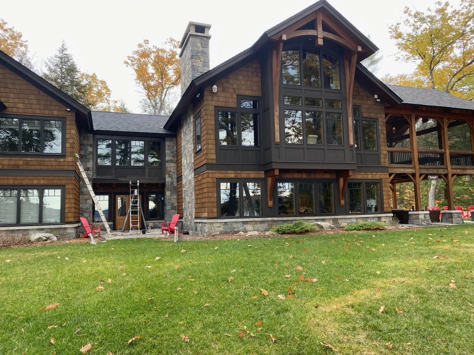 Modern home with cedar siding, dark trim, stone chimney, and covered porch overlooking lawn