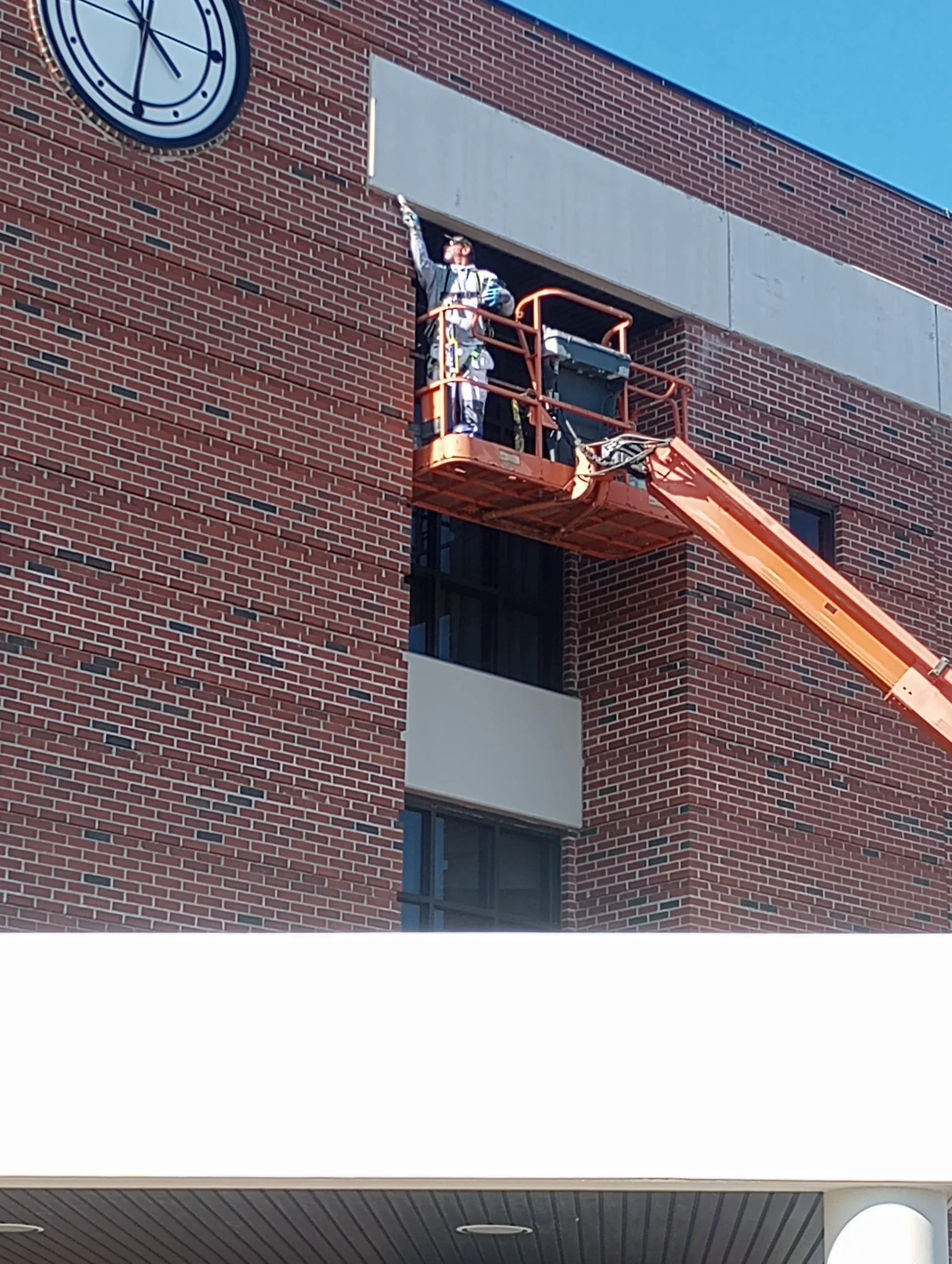 Worker on lift platform painting upper exterior of red brick commercial building
