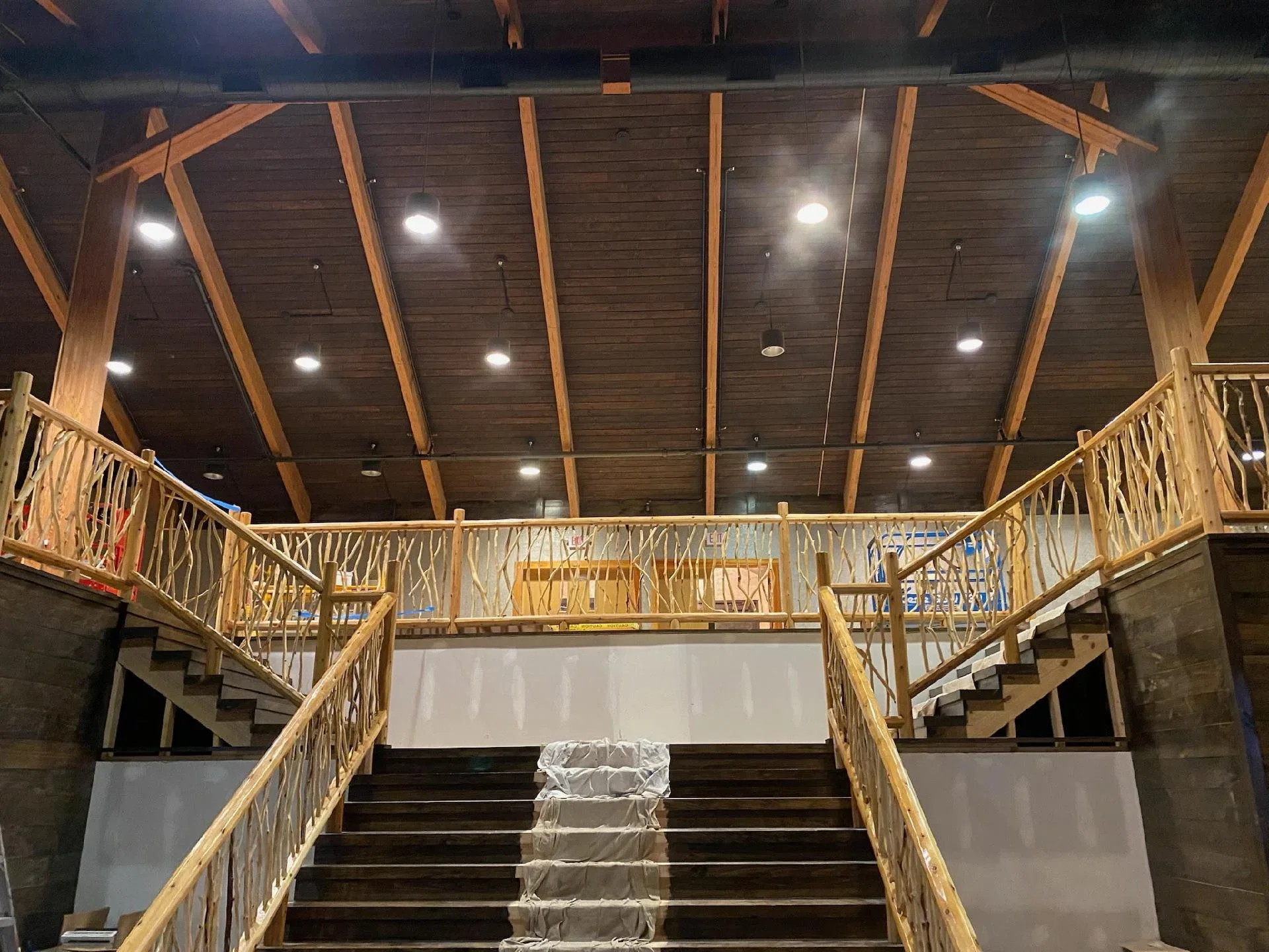 Commercial interior with painted drywall, wood beams, LED lighting, and wooden railings on multi-level staircase