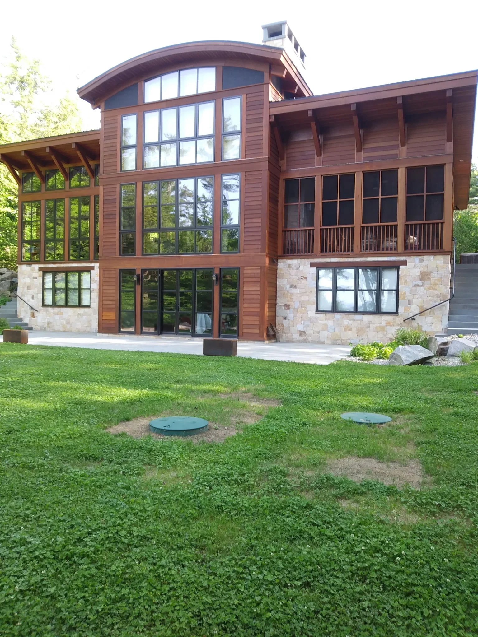 Modern home with brown cedar siding, large windows, stone base, and covered porch areas