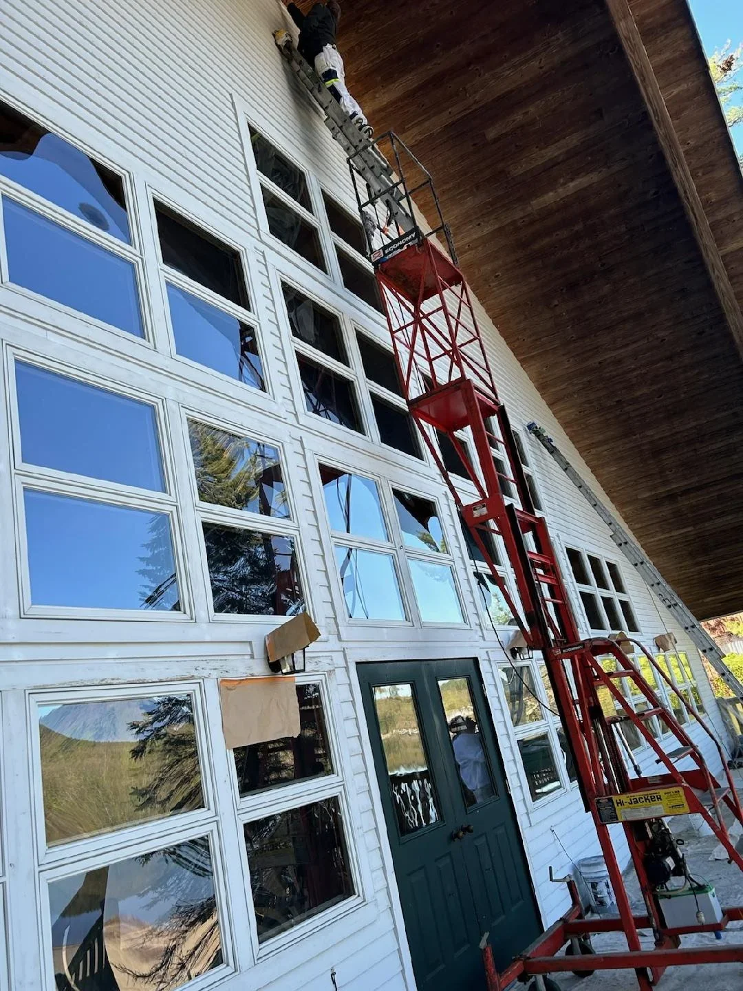 White painted house exterior with multiple windows and dark green door, painter on red lift